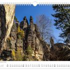 "Bizare Formationen in der Felsengasse im Bielatal. Augustkalender: Felsen, Bäume, blauer Himmel, steile Klippen."