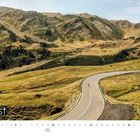Augustkalender mit Berglandschaft, kurvige Straße, grasbewachsene Hügel, vereinzelte Bäume im Hintergrund.