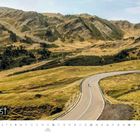 August, 2: Bundesfeiertag, 15: Maria Himmelfahrt. Eine kurvige Straße in einer hügeligen, grasbewachsenen Landschaft.