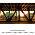 AUGUST in vier Sprachen oben; darunter ein Kalender. Ein Radfahrer unter einer Brücke, Sonnenuntergang und moderne Gebäude.