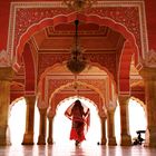 Dekorative rote und goldene Bögen mit feinen Verzierungen. Eine Person mit buntem Tuch schreitet durch die Halle.