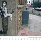Text: "anywhere". Wand-Graffiti zeigt eine stehende Person mit einem Schild. Umgebung ist eine städtische Straßenecke.