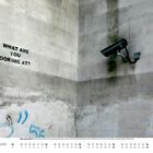„WHAT ARE YOU LOOKING AT?“ steht an der Wand neben einer Überwachungskamera. Es ist August im Kalender.