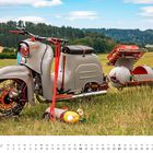 Ein grauer Motorroller mit Beiwagen steht auf einer Wiese. Unten steht "FEBRUAR" in einem Kalender.