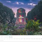 August 2027, Hamburg. Ein beleuchtetes Gebäude im Park, umgeben von Blumen und Bäumen bei Dämmerung.