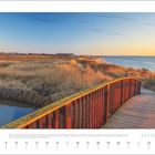 Kalenderseite mit August 2027. Ein Holzsteg führt über Marschland zu einem Strand mit Blick auf das Meer bei Sonnenaufgang.