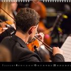 Kalender mit Musikern im Orchester, Geiger von hinten, umgeben von Noten und weiteren Musikern.