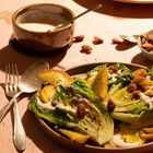 Salatteller mit Mandeln und gebratenen Kartoffeln, hellbraune Schale mit Dip, Löffel und Gabel auf hellem Tisch.