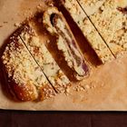 Ein Streuselkuchen, geschnitten, zeigt Füllung mit Kirschen auf braunem Backpapier, serviert auf einem Holzbrett.