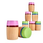Holzspielzeugfässer, bemalt mit rosa, grün und blauen Streifen, aufgestapelt und eines am Boden liegend.