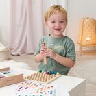 Ein Kind spielt fröhlich mit einem Montessori-Spielzeug auf einem Tisch, umgeben von bunten Mustervorlagen.
