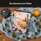 "Ein Moment zum Teilen." Puzzle-Schachtel auf einer Decke, umgeben von Efeu, Lichtern und einer brennenden Kerze.
