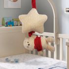 Ein Kinderzimmer mit Kuschelbär und Stern aus Plüsch, beide am Gitterbett befestigt; nahe ein Schnuller. Bücher im Hintergrund.