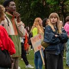 Ein Schild mit der Aufschrift "No Love Here" vor einer Gruppe junger Menschen in lässiger Kleidung auf einer Wiese.