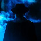 Ein mysteriöser Mann mit Hut in blauem Nebel, Gesicht im Schatten.