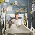 "Get Well Ricky" auf Poster. Mann im Krankenhausbett, lächelt, mit Getränk in der Hand. Ballons und Karten umgeben ihn.
