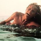 „8“ auf einer Boje sichtbar. Eine Frau im Wasser wirkt verzweifelt, umgeben von welligem Meer.