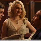 Drei Personen in eleganter Kleidung. Eine Frau mit blonden Locken trägt ein glitzerndes Kleid und Blumen im Haar.