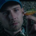 Es gibt keinen sichtbaren Text. Ein Mann in einer blauen Kappe betrachtet aufmerksam etwas Kleines, das er hält.