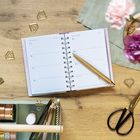 Text: „Februar 2027“, „Notizen“. Ein geöffneter Planer mit Stiftekasten und Schere auf Holzoberfläche.