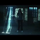 Eine Frau steht in einem dunklen, verlassenen Raum. Lichtstrahlen fallen durch Ritzen und beleuchten sie.