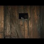Eine rustikale Holztür in einer Steinwand, ein kleines Fenster mit einer Figur und einer Pistole, die durchschaut.