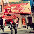 "LIBERATORS - PEOPLE OF AMERICA ARISE AND JOIN THE REVOLUTION" steht auf einem großen Banner. Soldaten auf der Straße.