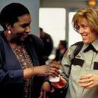 Zwei Frauen unterhalten sich lächelnd. Eine trägt eine Polizeiuniform mit Abzeichen, die andere ein buntes Oberteil.