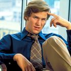 Ein Mann mit blauem Hemd und gemusterter Krawatte sitzt entspannt auf einem Stuhl und blickt nachdenklich.