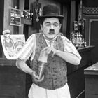 Schilder an der Wand: "SAN FELICE" und "SMOKE SAN FELICE". Ein Mann mit Melone und Schnurrbart mixt einen Drink an einer Theke.