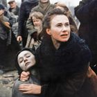 Eine Frau hält eine bleiche, bewusstlose Person im Arm. Um sie herum sind besorgte Menschen in Winterkleidung versammelt.