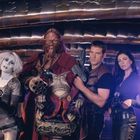 Vier Personen stehen nebeneinander, alle bewaffnet und in futuristischer Kleidung. Einer ist ein kleines, sitzendes Wesen.