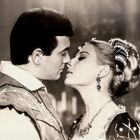 Zwei Personen in historischer Kleidung stehen sich nah gegenüber, fast in einem Kuss; romantische, intensive Stimmung.