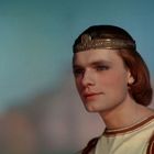 Ein Mann mit weichen Gesichtszügen trägt eine dekorative Krone und römische Robe, schaut ruhig in die Ferne.