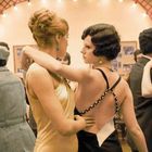 Eine Tanzszene mit Paaren in Abendgarderobe in einem festlich dekorierten Saal. Lichterkette im Hintergrund.