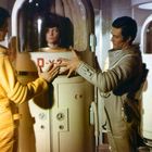 "D-X-2", "D-X-1" auf Raumkapseln. Zwei Menschen interagieren mit einer Person in einer Kapsel, sci-fi Ambiente.