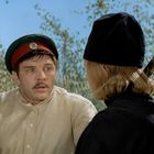 Zwei Männer in Uniformen sprechen im Freien; einer mit roter Mütze schaut überrascht, der andere trägt schwarz.