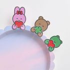 Illustration: Ein rosa Hase mit rotem Herz, ein brauner Bär mit grünem Kleeblatt, ein grüner Frosch mit rotem Herz auf einem pastellfarbenen Teller.