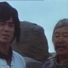 Zwei Männer stehen vor felsigem Hintergrund. Beide sehen in die Kamera; der linke trägt ein weißes Hemd, der rechte eine Brille.