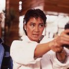 Zwei Frauen, eine zielt entschlossen mit einer Pistole, die andere schaut ernst, beide in moderner Kleidung.