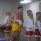 Ich kenne den Text nicht. Drei Personen in Cheerleader-Uniformen stehen in einem Raum mit einem Mann in gelber Sporthose.