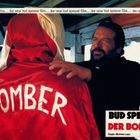 Text: "Bud Spencer Der Bomber." Ein Mann in rotem Mantel mit "Bomber" hinten, wird von einem anderen Mann angesehen.