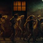 Eine Gruppe von Figuren in Bandagen und Kostümen bewegt sich in einem rostigen, düsteren Raum unter grellem Licht.