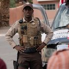 Ein Polizist mit der Aufschrift „M. Cooke“ steht vor einem Fahrzeug, das teilweise von Schildern verdeckt ist.