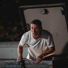 Ein Mann in einem weißen T-Shirt klettert durch eine Dachluke und hält etwas in der Hand. Es ist Nacht.