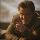 Keine sichtbaren Texte. Ein lächelnder Mann in warmer Beleuchtung, sitzt und zeigt freundlich mit dem Finger auf die Kamera.