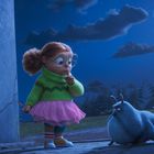 Eine animierte Szene zeigt ein Mädchen mit Brille und einem grünen Pullover, das einem blauen, tierähnlichen Wesen gegenübersteht.