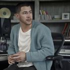 Ein Mann in einem Musikstudio sitzt vor einem Computer mit Audioprogramm, umgeben von Instrumenten und Lautsprechern.