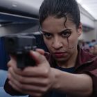 Eine Frau im Flugzeug zielt mit einer Waffe, entschlossener Gesichtsausdruck, Passagiere im Hintergrund.