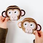 Zwei Hände halten Papiermasken in Form von Affengesichtern mit großen Augen und freundlichem Ausdruck.